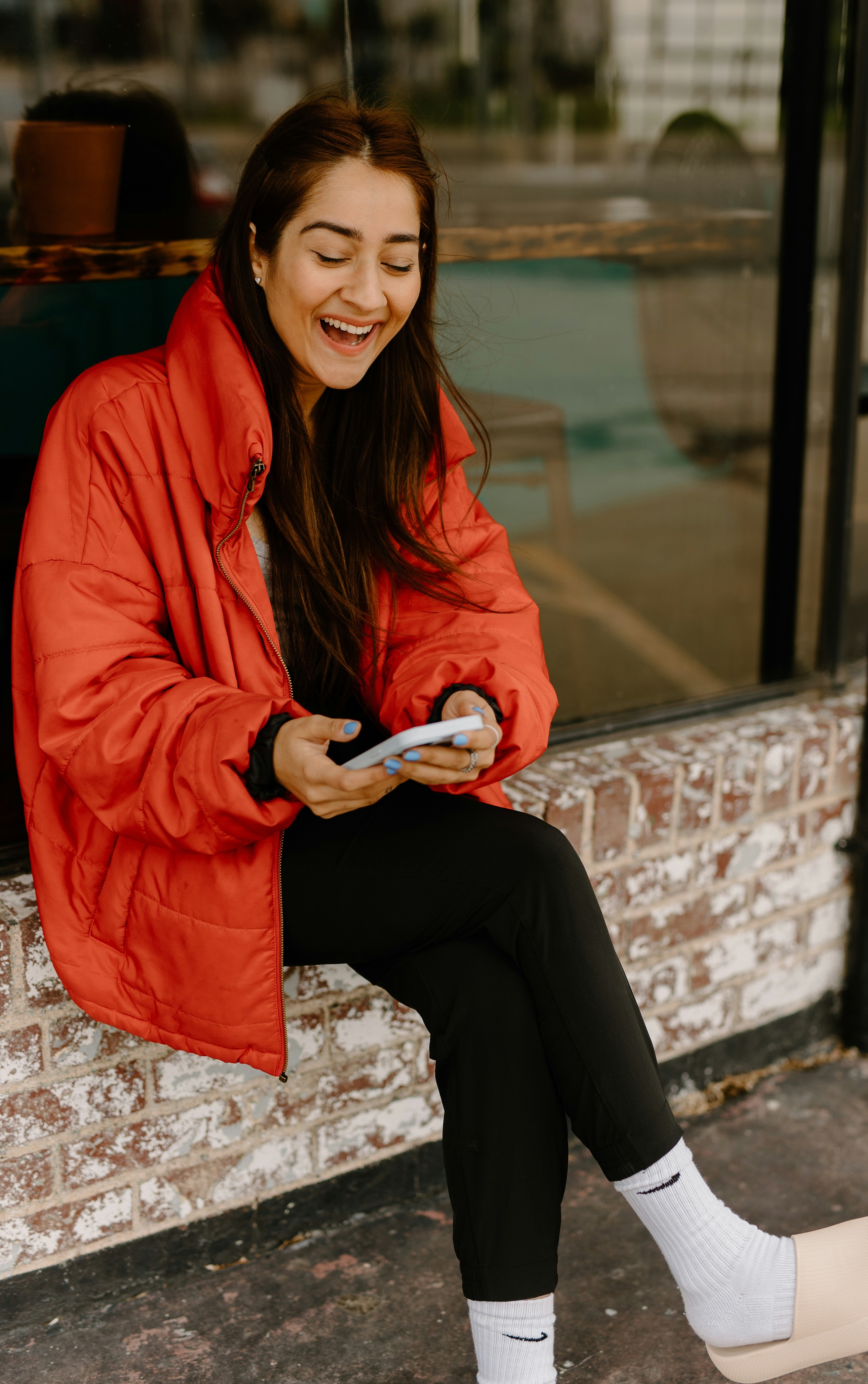 Woman laughing while looking at her phone, wearing a red coat