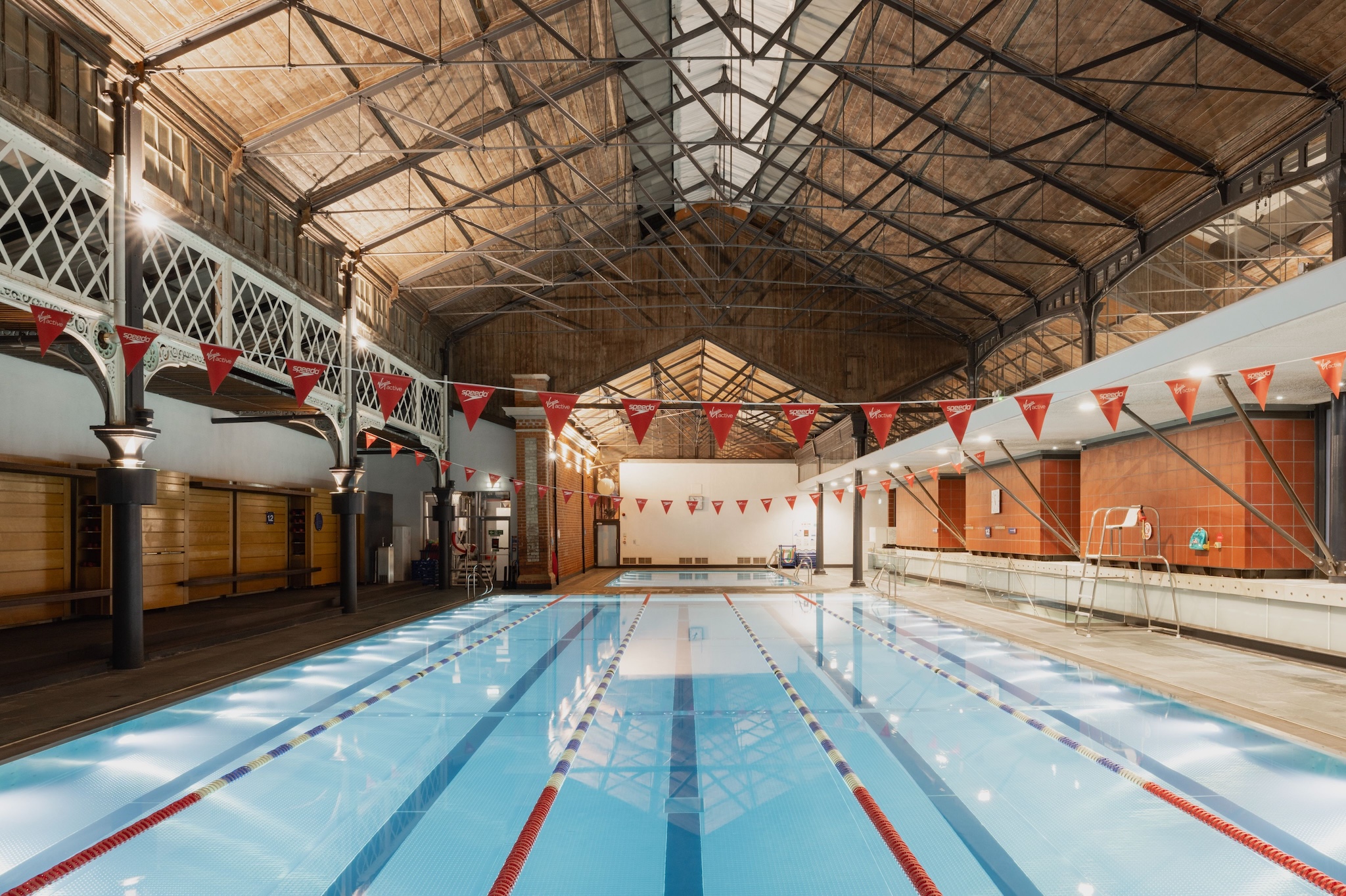 Grand Victorian-era indoor swimming pool at a Virgin Active club, with red pennant flags strung beneath the vaulted roof